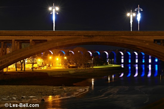View from Berwick Old Bridge to the Royal Tweed Bridge and the floodlit arches of the Royal Border Bridge.