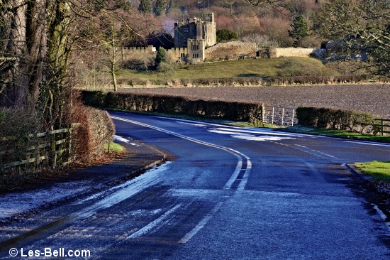 View to Bothal Castle with smoke behind it and a frosty road in the foreground.